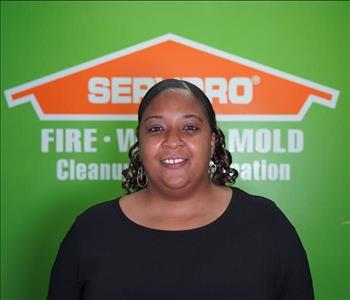 A woman standing in front of a green wall with a SERVPRO logo.  