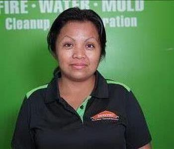 A woman standing in front of a green wall with a SERVPRO logo.  